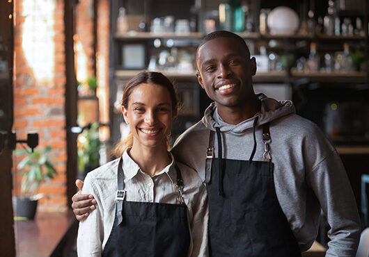 Happy diverse waiter and waitress looking at camera in restaurant